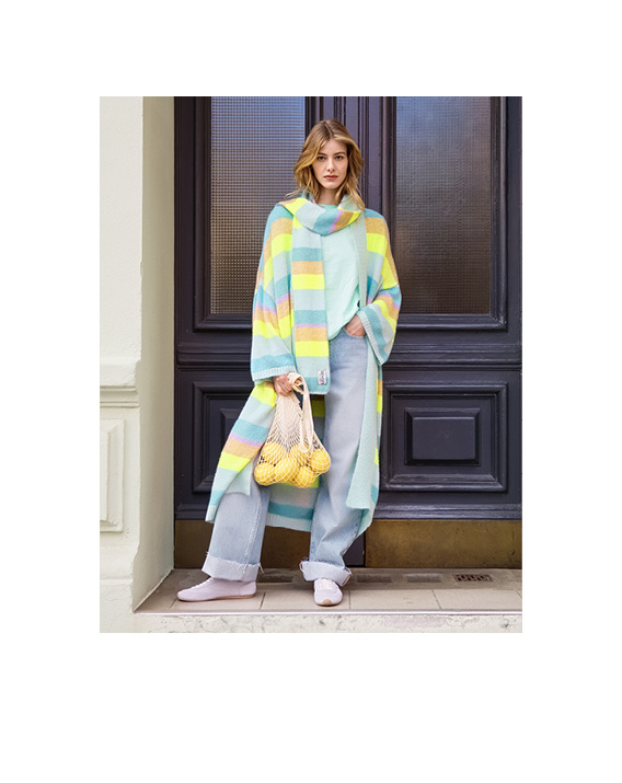 Model trägt bunten Cardigan und steht vor einer Holztür